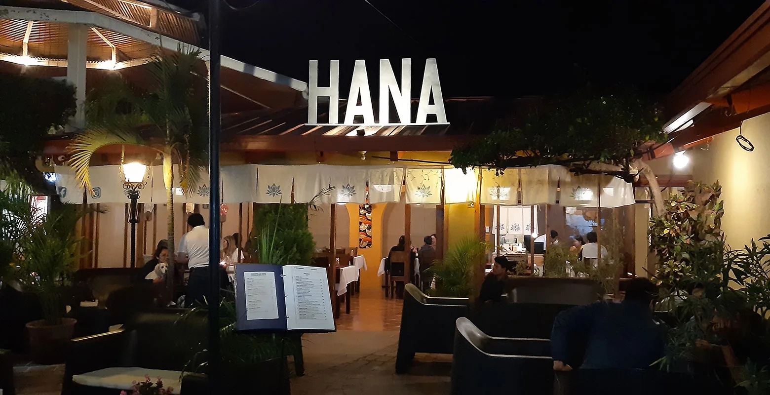 La entrada de Restaurante Hana de noche, con el letrero HANA iluminado