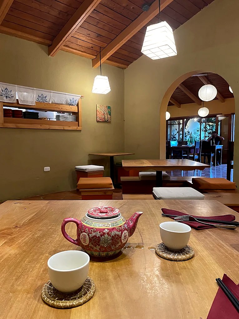 Una tetera y dos tazas sobre una mesa de madera, con el arco hacia el jardín al fondo