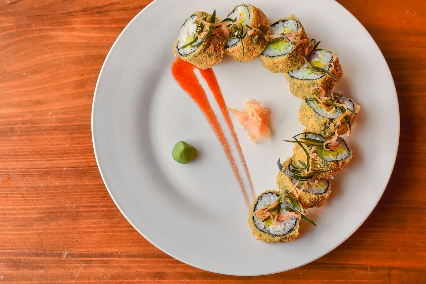 Rollo de sushi empanizado, servido en curva sobre un plato blanco con jengibre y wasabi